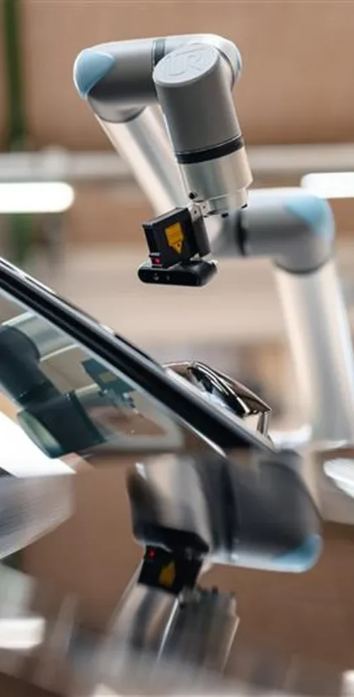Brazo robótico colaborativo (cobot) equipado con un sistema de visión artificial inspeccionando el parabrisas de un coche negro en un taller industrial.